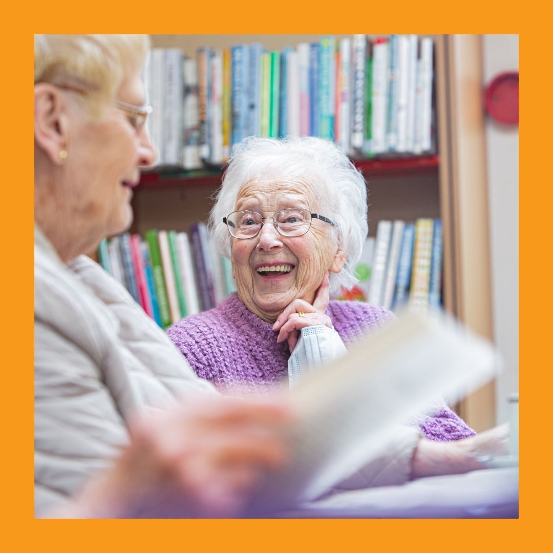A photo of two women with white hair sitting around a table laughing
