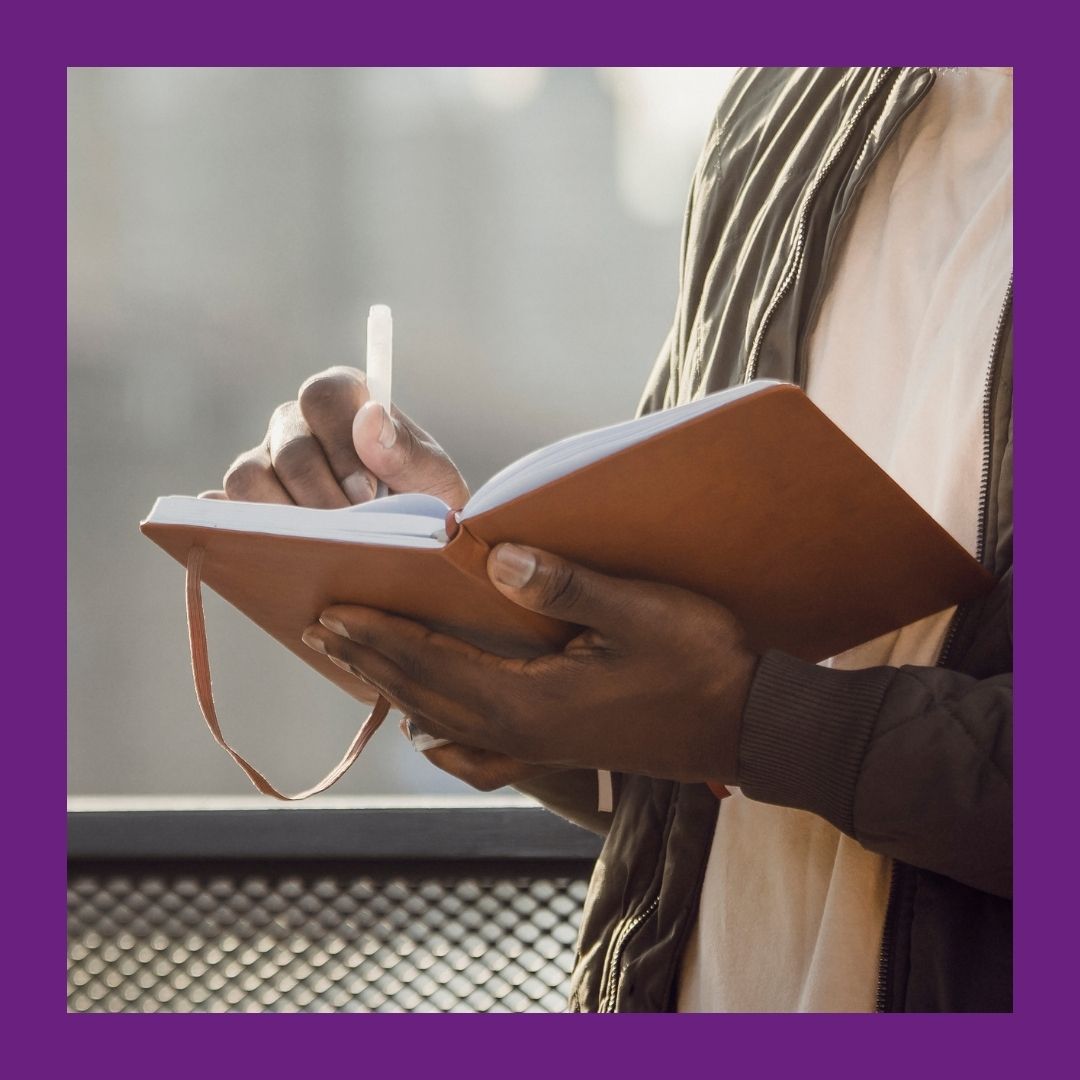 A photo of a man from the chest down holding an open notebook and a pen