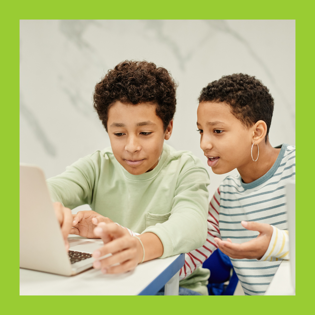 And adult and child sat at a laptop, the adult is calmly explaining something to the child