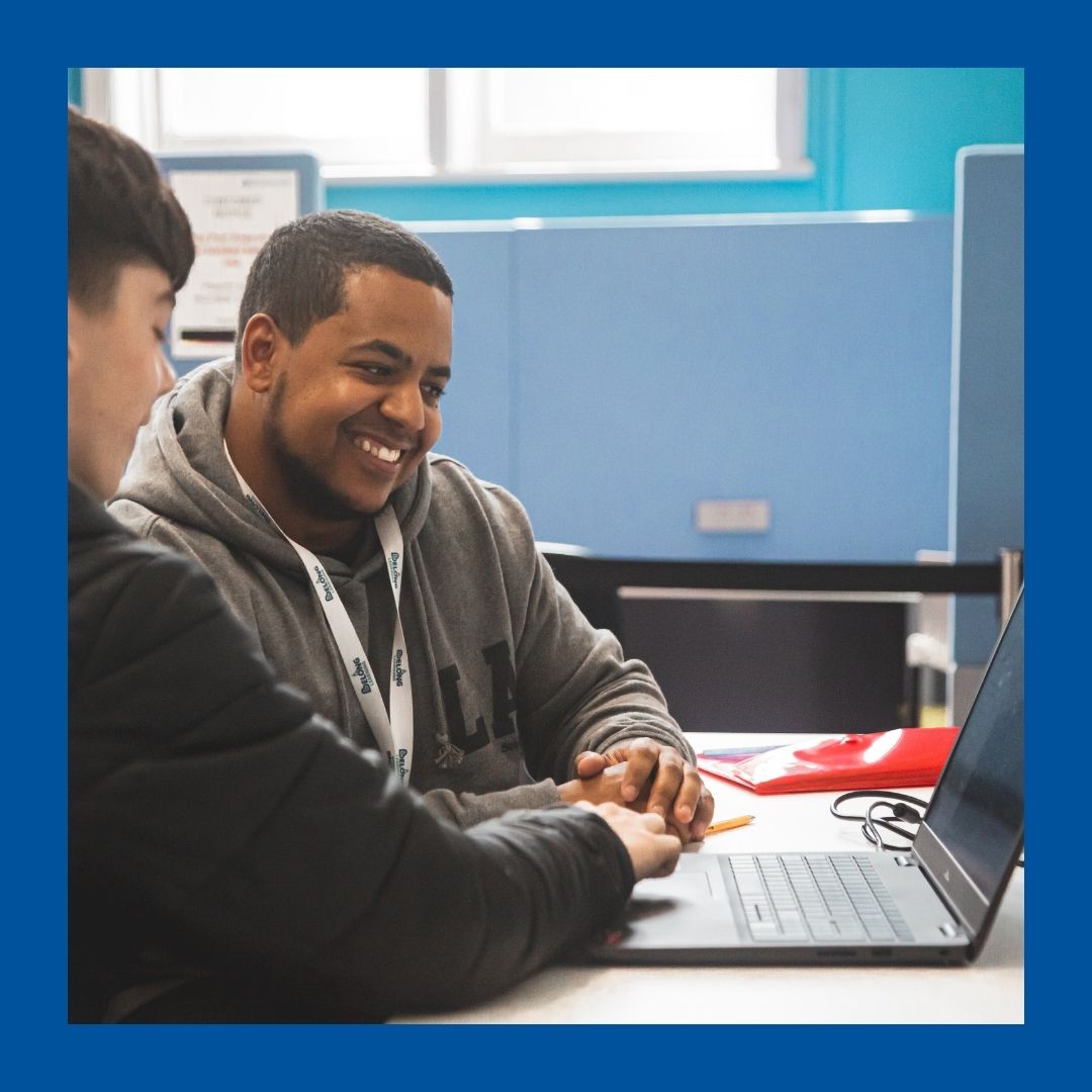 Two people smiling as they work at a laptop together.