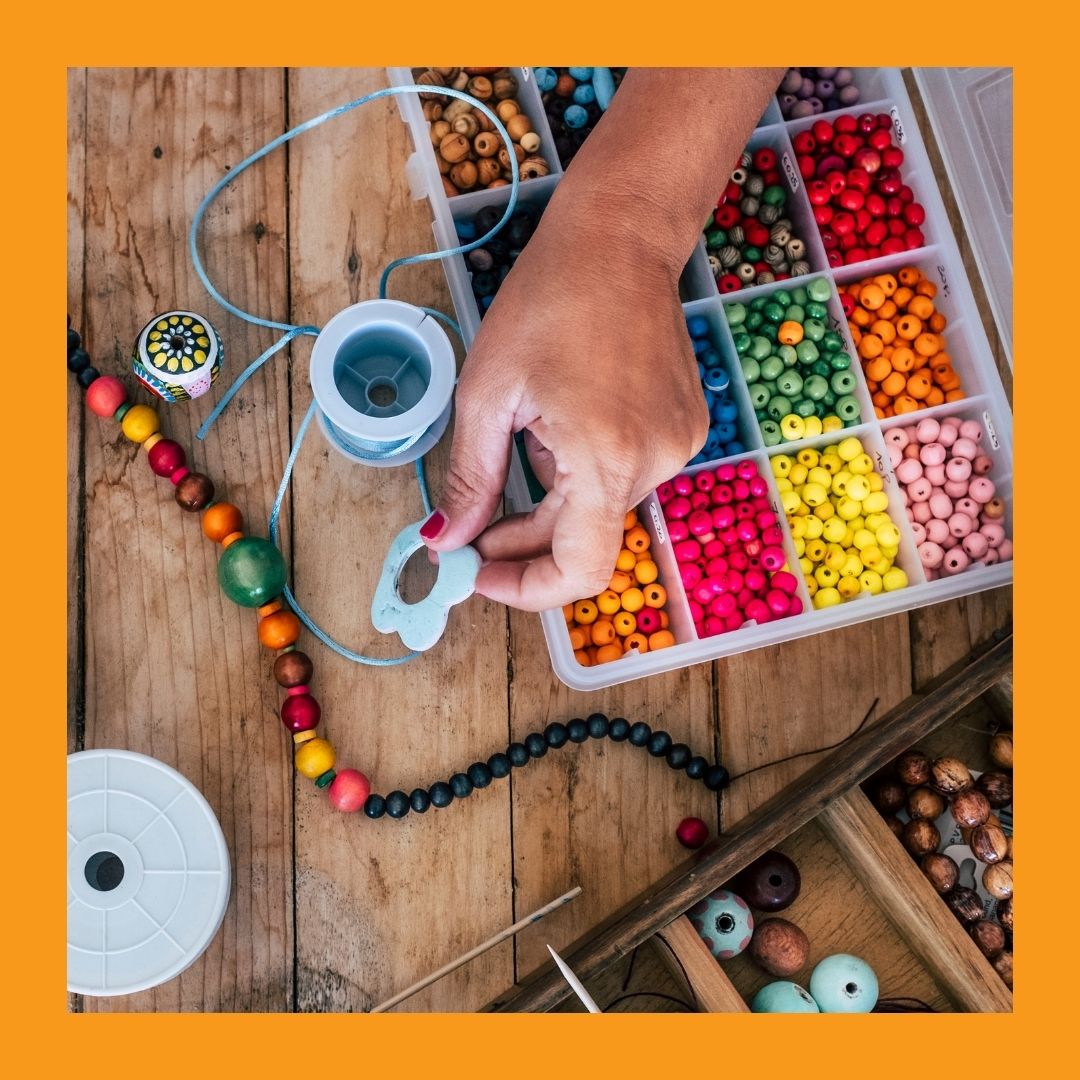A photo of a hand picking up a tool from a table full of colourful beads