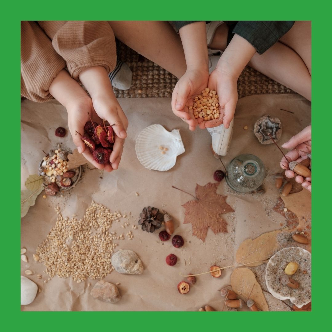 A photo from above of two children sitting at a mat covered in natural items such as leaves and seeds