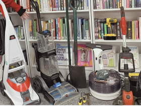 Collection of tools and household items in front of library book shelves with a person standing next to them