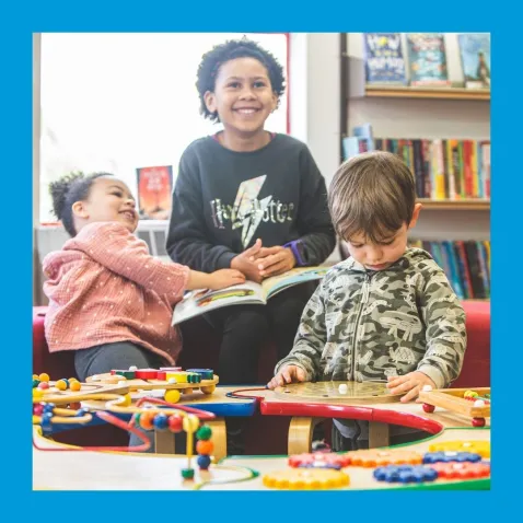 A child and two pre-schoolers enjoy books and table manipulatives in a library