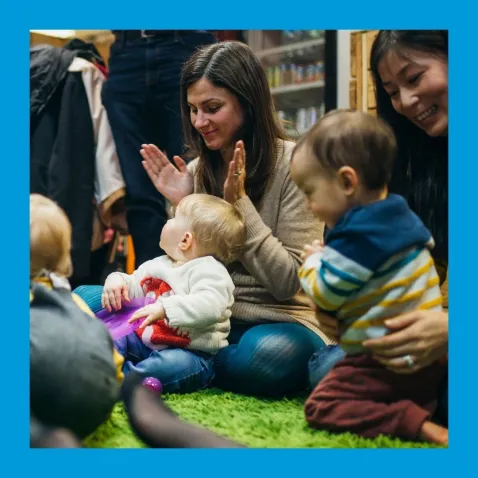 A lady clapping and smiling at a baby on her lap.