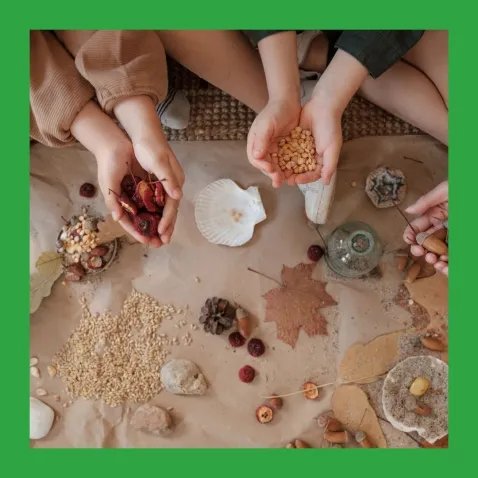 A photo from above of two children sitting at a mat covered in natural items such as leaves and seeds