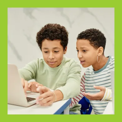 And adult and child sat at a laptop, the adult is calmly explaining something to the child