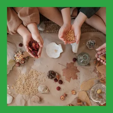 A photo from above of two children sitting at a mat covered in natural items such as leaves and seeds