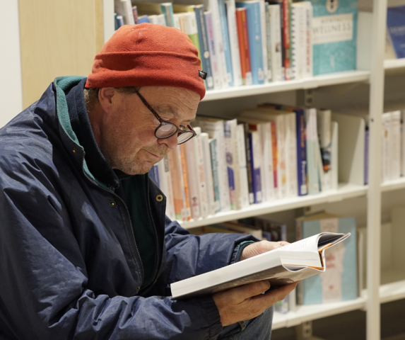 A man in a blue coat and orange hat enjoying a non-fiction book