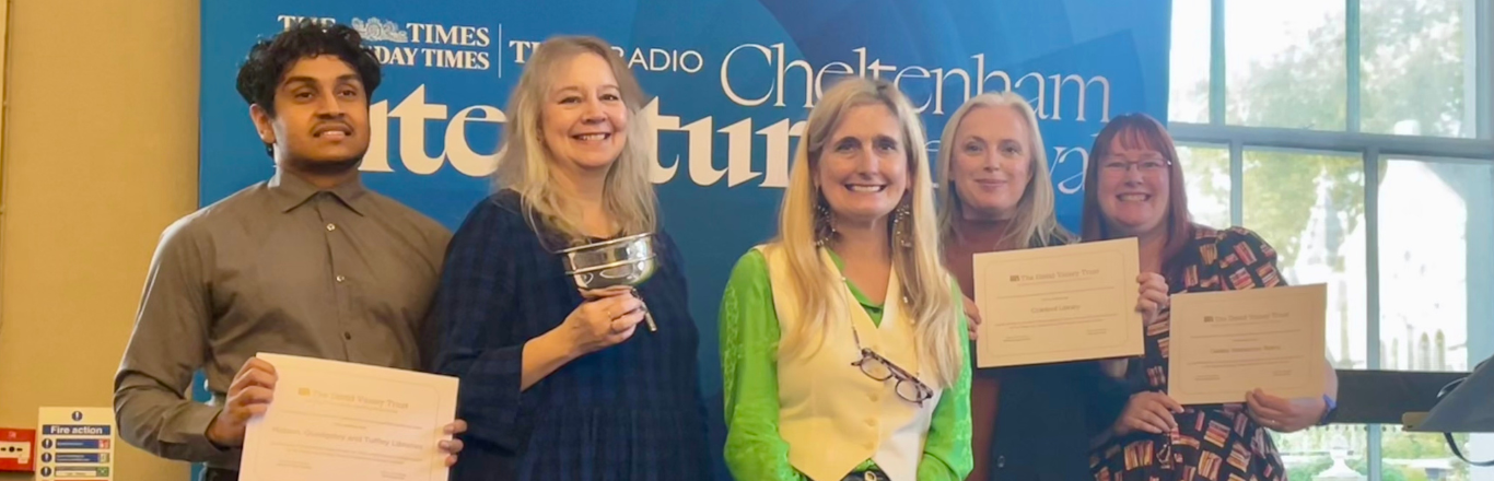 Four library staff lined up on either side of author Cressida Cowell, holding certificates and a trophy.