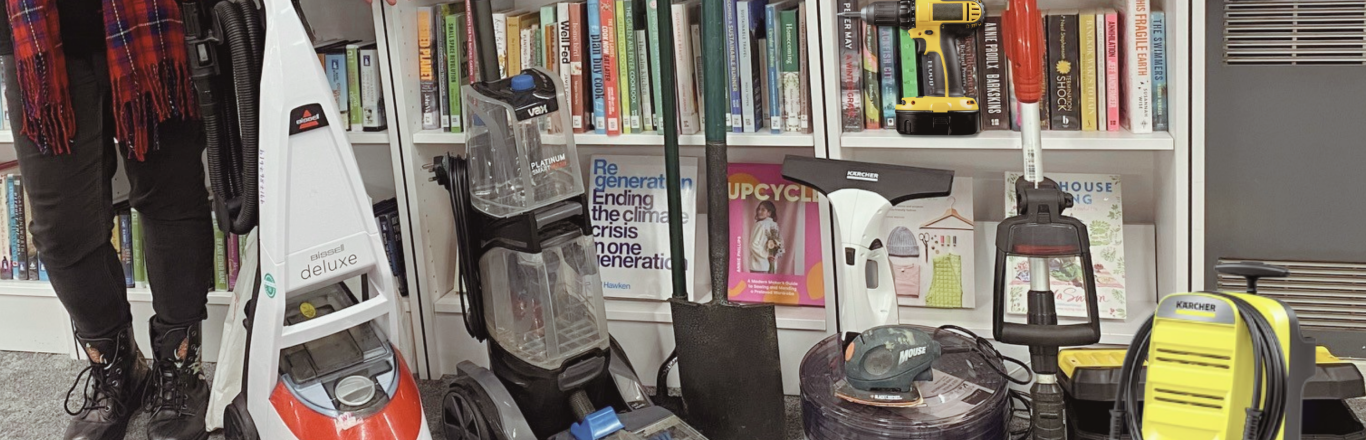 Collection of tools and household items in front of library book shelves with a person standing next to them